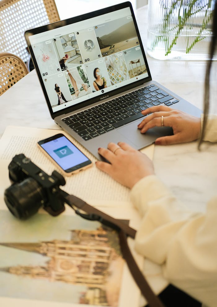 A woman working on a laptop with a camera and smartphone on the desk in a cozy indoor setting.