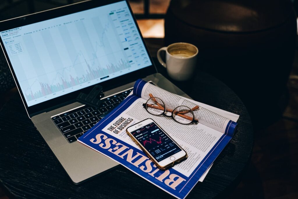 A professional workspace featuring a laptop, smartphone, coffee cup, and business magazine on a table.